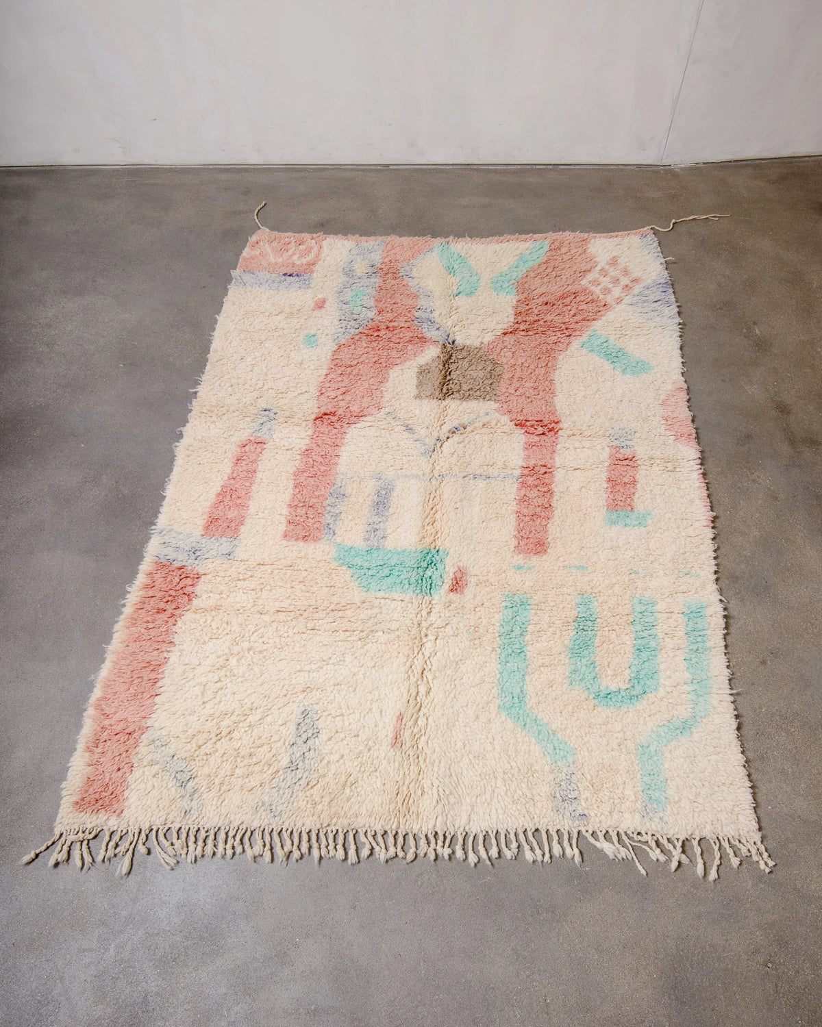 Berberlin Vintage Berber Rug made of fluffy cream, turquoise, faded red and purple wool, laying flat on a grey concrete floor.